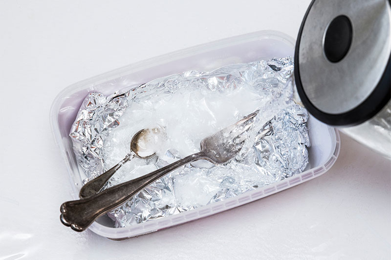 A solution of baking soda(Sodium bicarbonate) and warm water will remove the tarnish from silver when the silver is in contact with a piece of aluminium tin foil. Pouring hot water over silver.